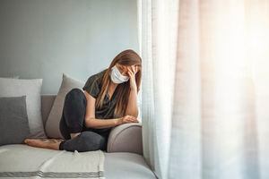 Triste niña solitaria quedarse aislada quedarse en casa con una máscara médica protectora estéril en la cara mirando a la ventana, mujer aburrida debido al coronavirus pandémico chino covid-19.  Cuarentena, prevenir infecciones