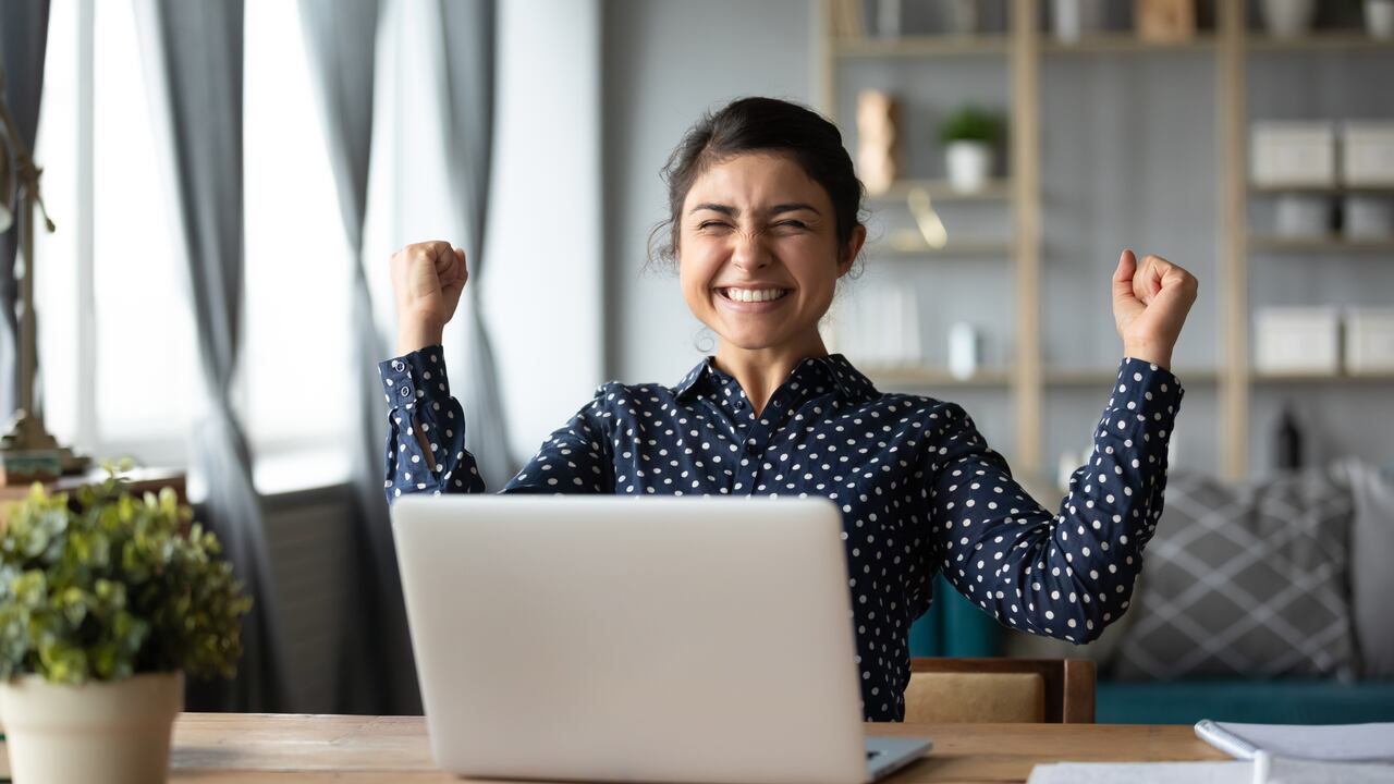 Eufórico mujer estudiante indio ganadora celebrar victoria triunfo sentarse en casa escritorio con computadora portátil ganar fortuna en línea sentirse emocionado obtener nueva oportunidad de trabajo buen examen resultado gran concepto de noticias