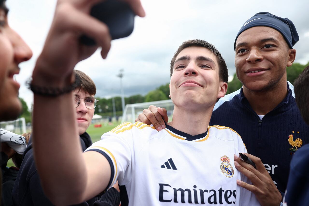 France's forward Kylian Mbappe (R) poses for a selfie photograph with a fan wearing a Real Madrid jersey, ahead of a training session, as part of the team's preparation for upcoming UEFA Euro 2024 Football Championship, in Clairefontaine-en-Yvelines on May 30, 2024. The UEFA Euro 2024 championship will take place from June 14 to July 14, 2024 in Germany. (Photo by FRANCK FIFE / AFP)