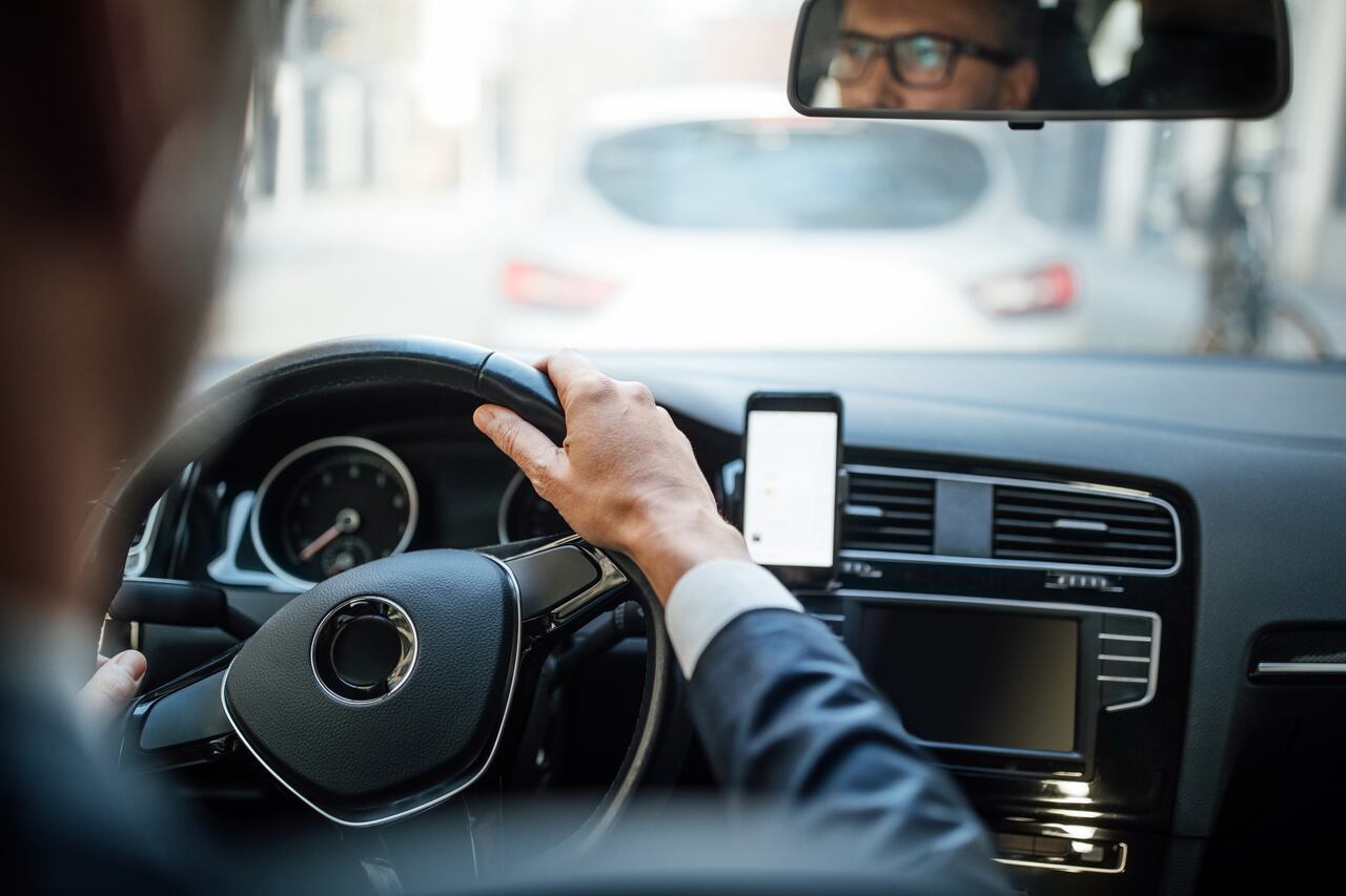 Mature man behind the steering wheel of a car with a mobile phone on the dashboard. Cropped shot of a businessman driving the car.