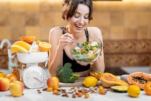 Mujer de deportes comiendo ensalada, de pie con una gran cantidad de alimentos frescos y saludables en la cocina. Concepto de adelgazamiento, deporte y alimentación saludable.