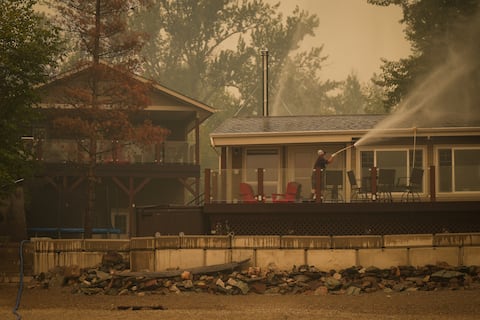 Trevor Manzuik, quien fue evacuado de su vivienda debido a un incendio forestal, rocía su propiedad luego de regresar a casa en bote, el domingo 20 de agosto de 2023, en la Columbia Británica, Canadá.