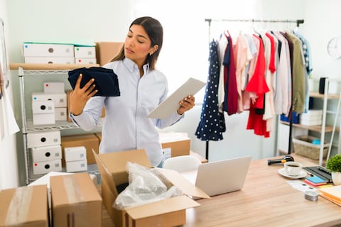 Female entrepreneur working on her business start-up and unpacking boxes from her suppliers for the online clothing shop