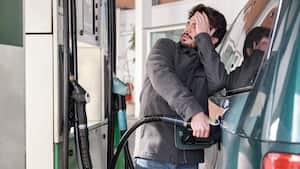 Joven repostando su vehículo mientras mira preocupado por los altos precios de la gasolina.