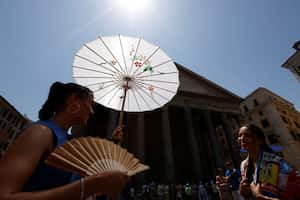 Una mujer se protege del sol bajo una sombrilla y usa un abanico plegable cerca del Panteón durante una ola de calor en Italia, en Roma