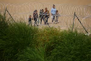 Migrantes pasan junto a una valla de alambre de púas desplegada para impedir el cruce de migrantes a Estados Unidos, vista desde Ciudad Juárez, México, el 28 de agosto de 2023.