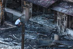 Un hombre mira hacia un helicóptero que pasa mientras se agacha cerca de un edificio destruido en el centro. (Robert Gauthier/Los Ángeles Times a través de Getty Images)