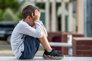 Crestfallen Crying child boy sitting at the schoolyard covering his face