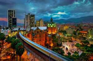 El metro elevado de Medellín está en movimiento mientras se precipita hacia la estación Parque Berrio frente al iluminado Palacio de la Cultura en la Plaza Botero en Medellín, Colombia. La Ciudad de la Eterna Primavera está ubicada en el Valle de Aburrá, una región central de la Cordillera de los Andes en América del Sur.