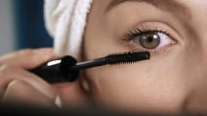 Girl paints eyelashes. Macro shot of face of attractive girl who puts black mascara on her eyelashes. Make-up artist, beauty, body care, facial cleansing, makeup, preparation for date or celebration concept. Close-up view
