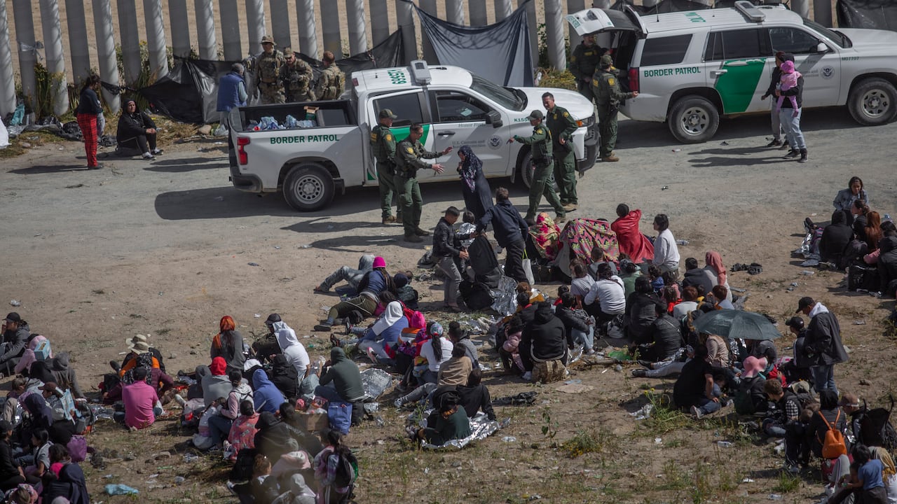 Los migrantes se sientan en filas frente a las fuerzas de seguridad estadounidenses en el área entre los dos muros que separan a México de los Estados Unidos.
