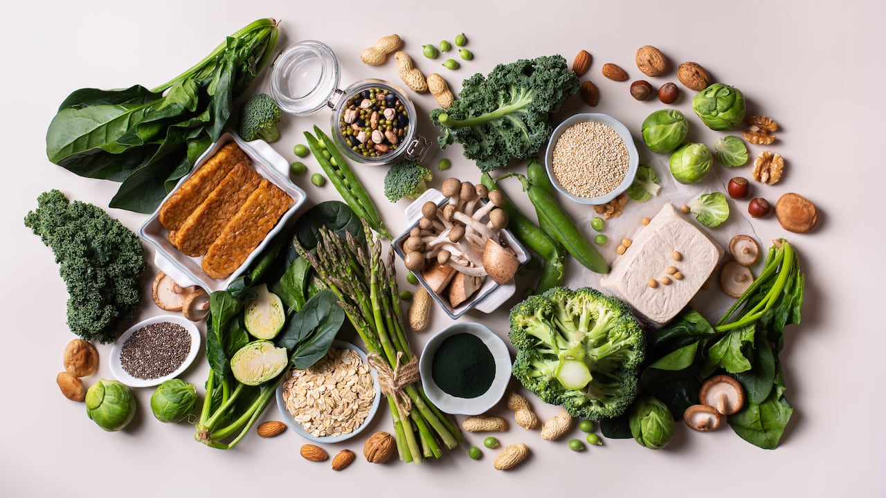 Variedad de alimentos veganos saludables, fuentes de proteínas a base de plantas y alimentos para la construcción del cuerpo. Tofu soja tempeh, vegetales verdes, nueces, semillas, harina de avena con quinua y espirulina. Vista desde arriba
