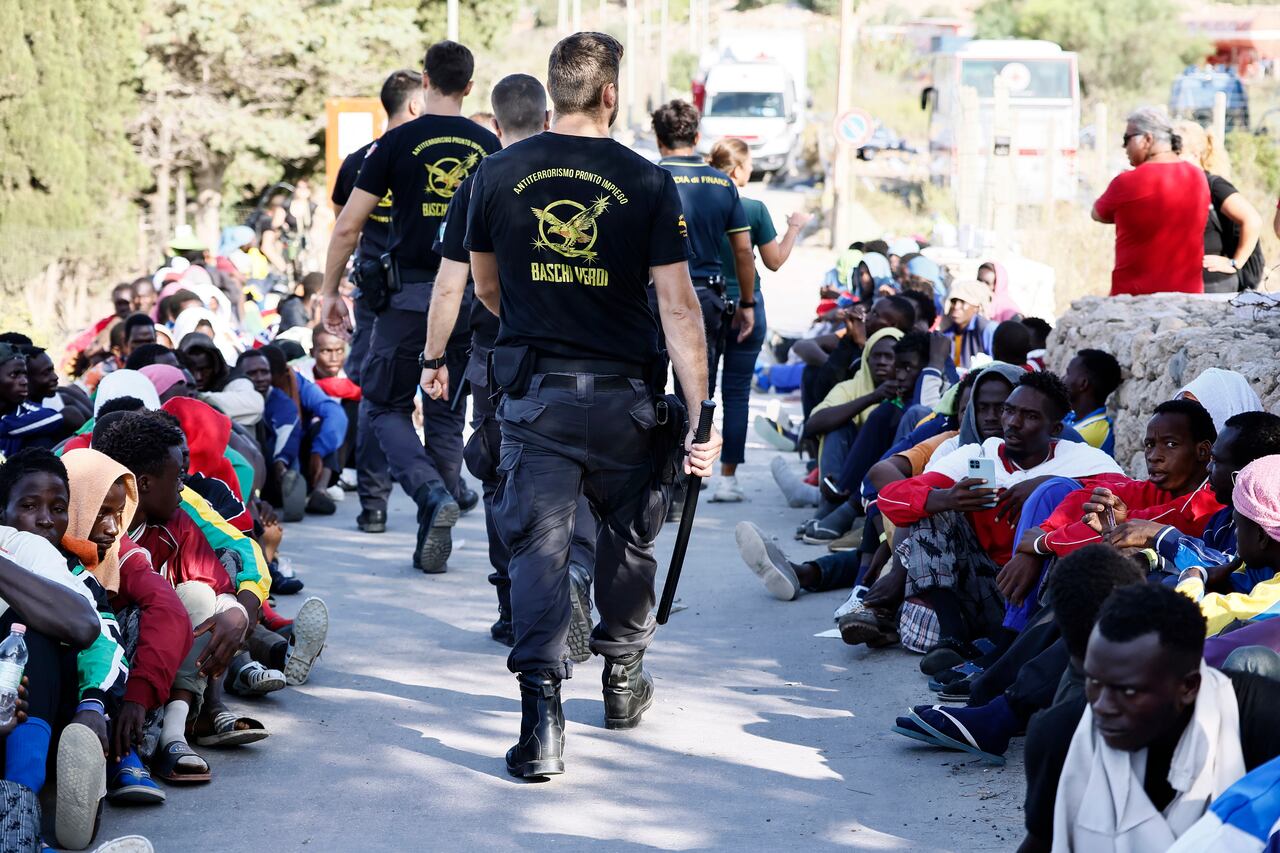 Agentes de policía caminan junto a inmigrantes en la isla de Lampedusa, Italia, el viernes 15 de septiembre de 2023. Lampedusa, que está más cerca de África que del continente italiano, se ha visto abrumada esta semana por miles de personas que esperan llegar a Europa desde Túnez, que ha reemplazó a Libia como la principal base de operaciones para las operaciones de tráfico de migrantes en el Mediterráneo. (Cecilia Fabiano/LaPresse vía AP)