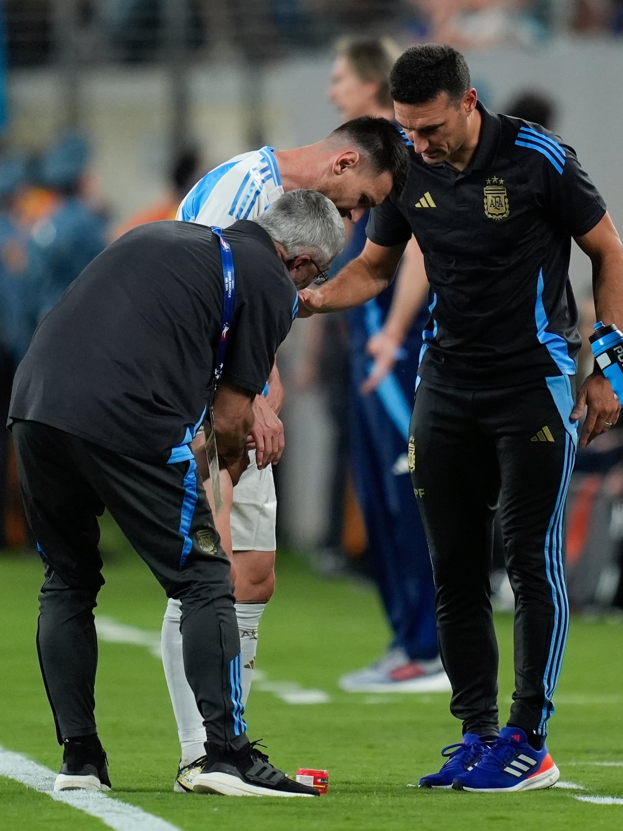 Argentina's coach Lionel Scaloni, right, and and a team assistant tend to Lionel Messi during a Copa America Group A soccer match against Chile in East Rutherford, N.J., Tuesday, June 25, 2024. (AP Photo/Julia Nikhinson)