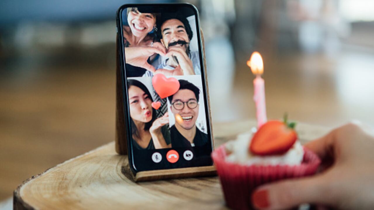 Close-up shot of a birthday cake and a smart phone screen showing international friends having a virtual birthday party on video call.