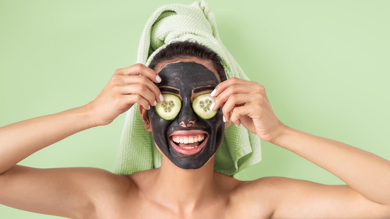 Happy smiling girl applying facial carbon mask portrait - Young woman having skin care cleanser spa day - Healthy beauty clean treatment and and self care lifestyle concept - Green background