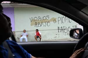 Se muestran personas junto a un graffiti que dice "Ventanas abajo o plomo FARC EP", que se refiere al grupo guerrillero Fuerzas Armadas Revolucionarias de Colombia, Ejército del Pueblo, en Corinto, provincia de Valle del Cauca, Colombia, el 6 de junio de 2024. (Foto de JOAQUÍN SARMIENTO / AFP)