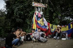 ARCHIVO - Migrantes sentados bajo un cartel que marca la frontera entre Panamá y Colombia durante su viaje a través del Tapón del Darién, el 9 de mayo de 2023. Abrumado por el resurgimiento de migrantes que cruzan la selva del Darién en la frontera con Colombia, el gobierno de Panamá anunció el jueves 24 de agosto de 2023 que tomará medidas concretas. (AP Foto/Iván Valencia, Archivo)