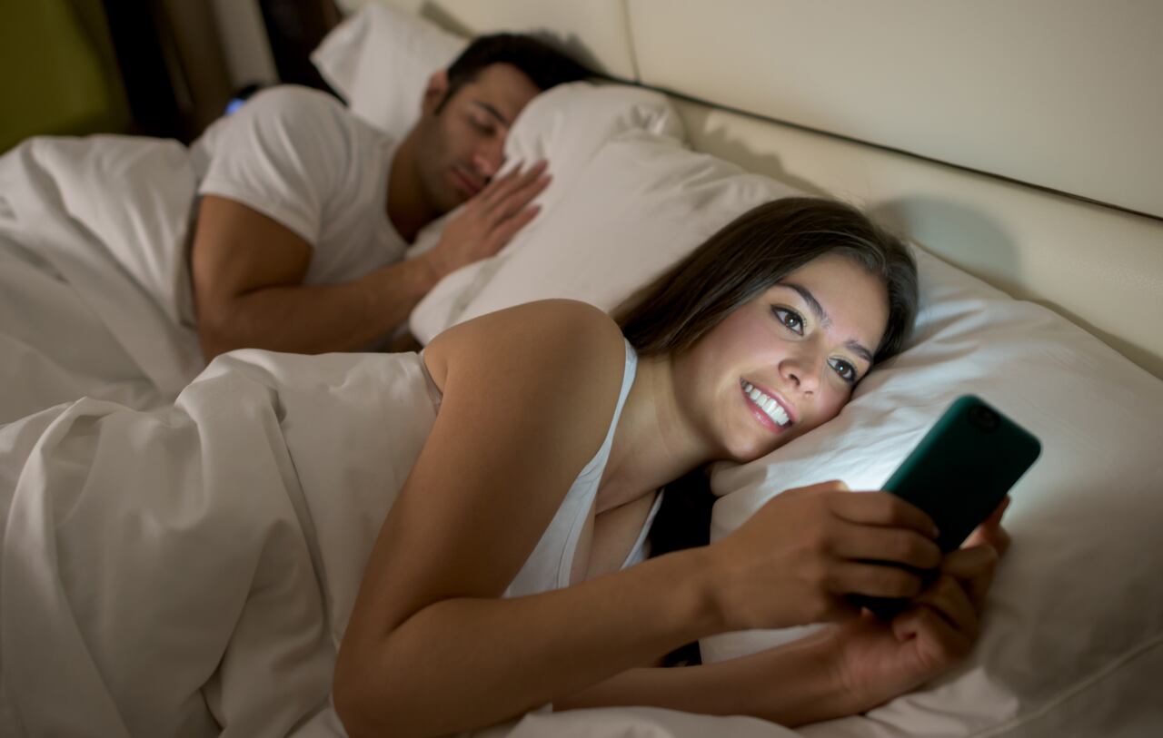 Mujer joven en redes sociales en la cama mientras su novio duerme